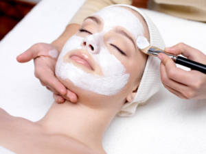 Beautiful young woman receiving facial mask at beauty salon - indoors